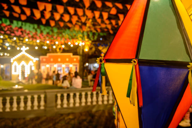 Lanterna colorida típica das festas juninas em destaque, com bandeirinhas decorativas e iluminação festiva ao fundo durante uma celebração de São João à noite.