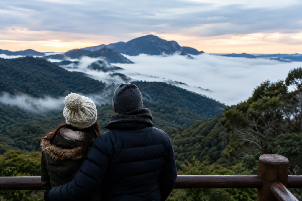Casal observando montanhas cobertas por neblina durante viagem de inverno na serra brasileira.
