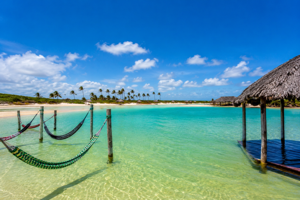 Lagoa cristalina em Jericoacoara com águas azul-turquesa, redes suspensas sobre a água e céu ensolarado, retratando um dos cenários mais paradisíacos do destino.